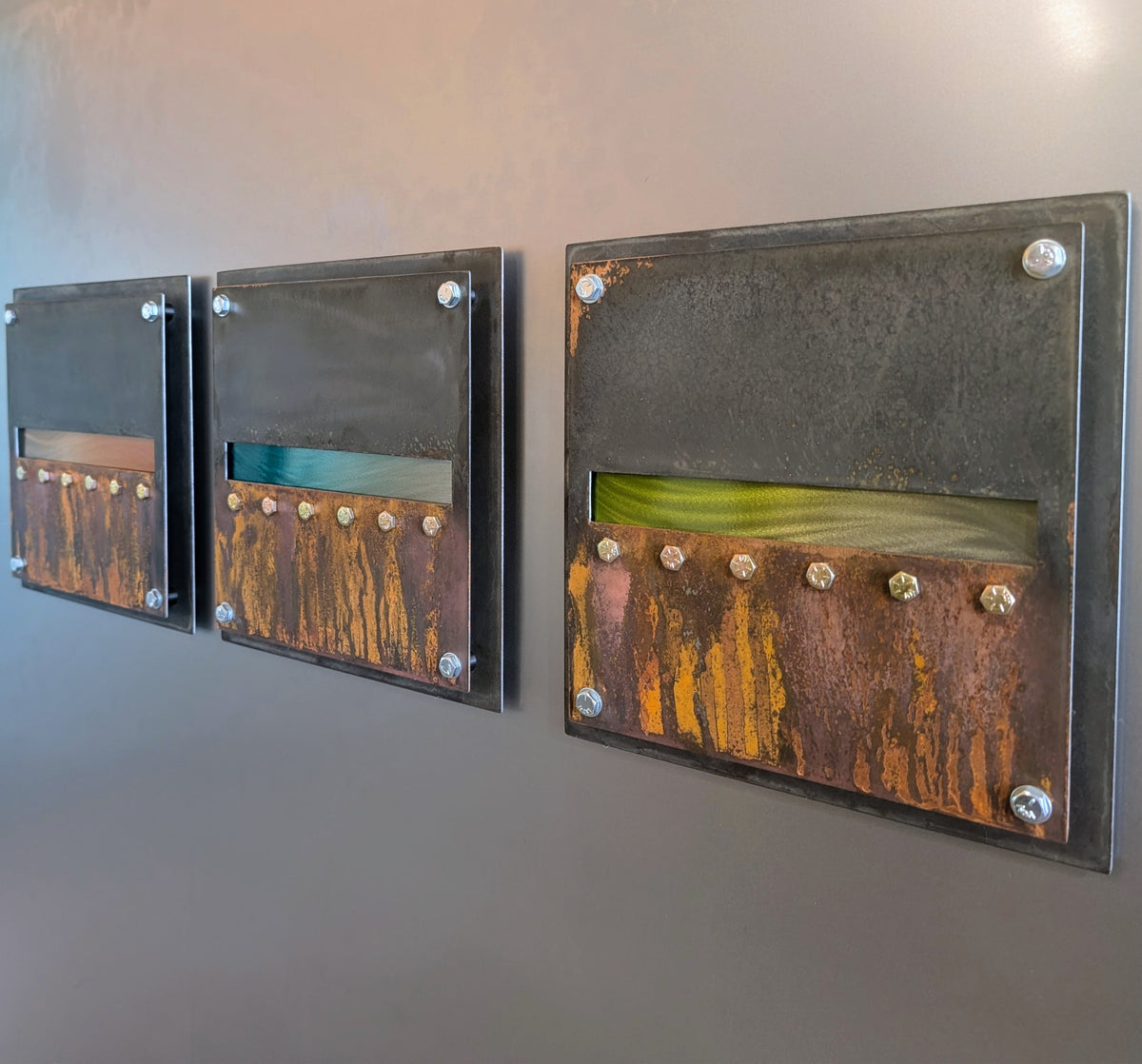 Angled view of the three panels, focused on the absinthe green horizon band, showing the layered steel edges and the rust texture