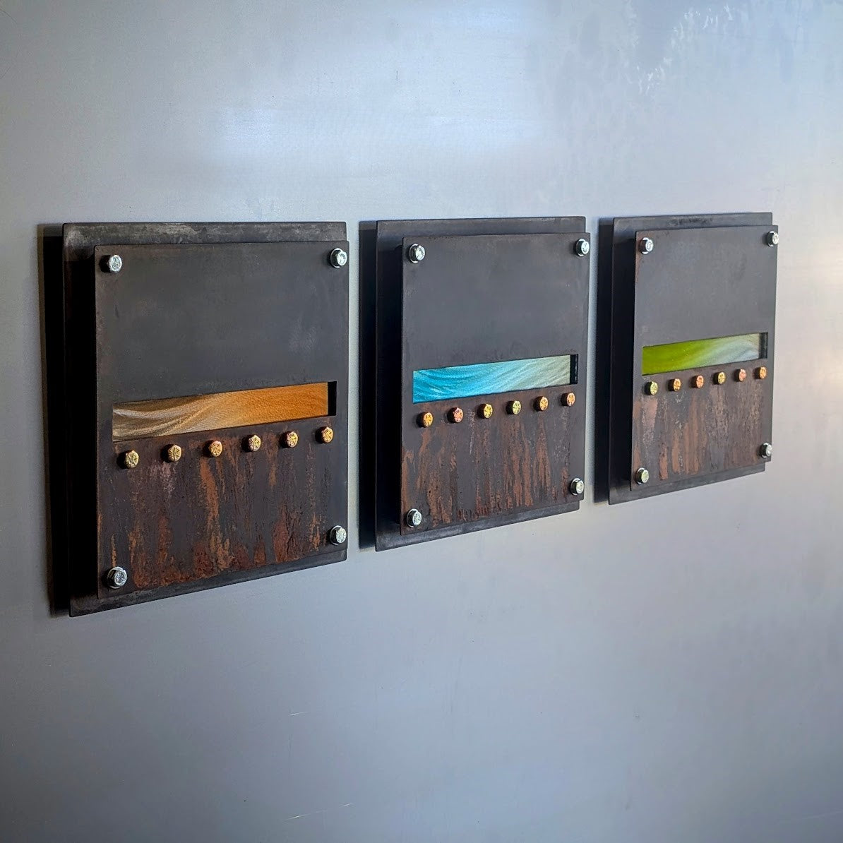Angled view of the three panels, focused on the absinthe green horizon band, showing the layered steel edges and the rust texture.
