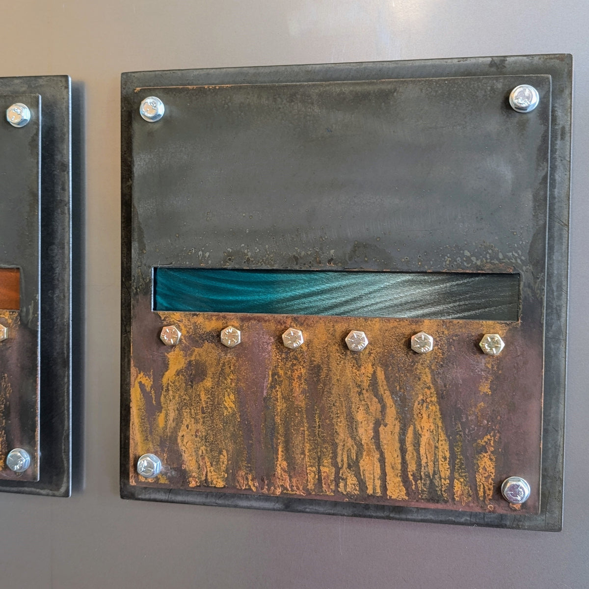 Detail of one panel: dark steel on top, a polished teal horizon band in the middle, and dripping orange rust below a row of hex bolts.