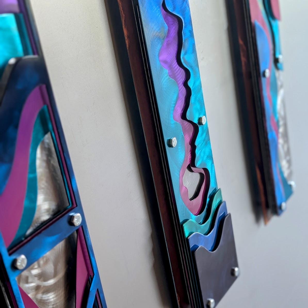  Side angle of the three Confluence panels on a wall, showing the stacked steel layers and dark rusted frame edges.